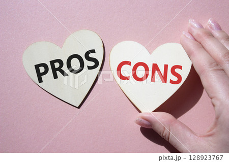 Pros vs Cons symbol. Concept word Pros vs Cons on wooden hearts. Businessman hand. Beautiful pink background. Business and Pros vs Cons concept. Copy space 128923767