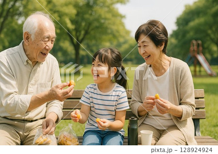 祖父母と孫が公園のベンチでおやつを楽しむ家族の交流シーン 128924924