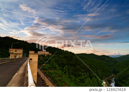 2025年布目ダムの夏　徐々に暮れていく夕焼け空　堰堤と布目川の谷を黄金色に染める黄金雲 128925628