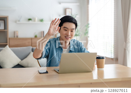Happy young Asian man working on laptop in living room 128927011