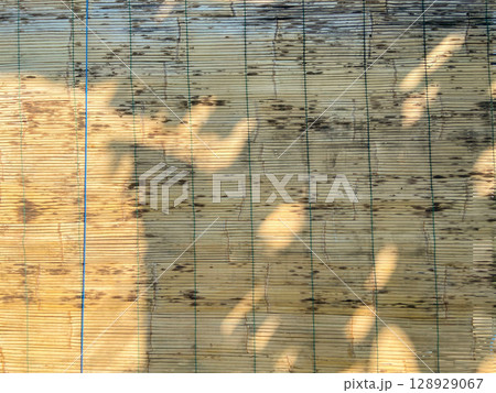 Wooden wall with bamboo blinds in the sunlight. Abstract background. Wooden wall with bamboo blinds in the sunlight. Abstract background. 128929067