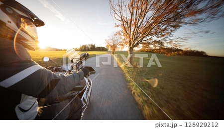 Driver riding motorcycle on empty road during sunset , view from the passenger side 128929212