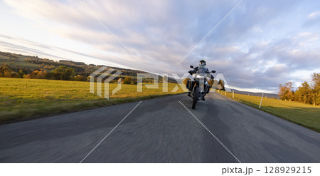 Driver riding motorcycle on empty road during sunset, autumn mountains Driver riding motorcycle on empty road during sunset, autumn mountains 128929215