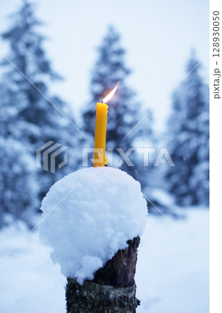 Candle is lit on top of a snow-covered log 128930050