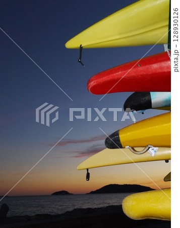 Row of kayaks are lined up on a dock, with the sun setting in the background 128930126