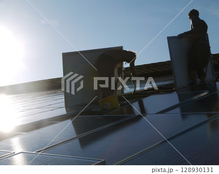 Two men are working on a roof, one of them is holding a bucket 128930131