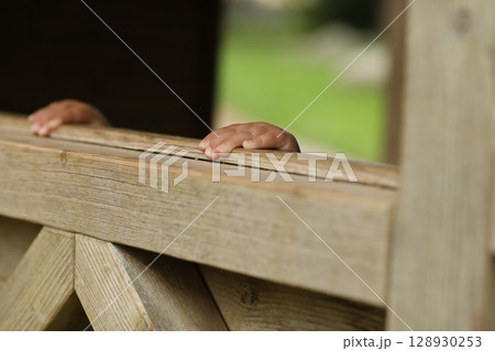 A wooden fence with two hands peeking out from behind it 128930253