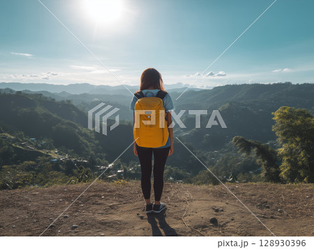 girl with backpack stands on top of hill, feeling happy and free, gazing at serene mountain range under bright sun, enjoying scenic vista girl with backpack stands on top of hill, feeling happy and free, gazing at serene mountain range under bright sun, enjoying scenic vista 128930396