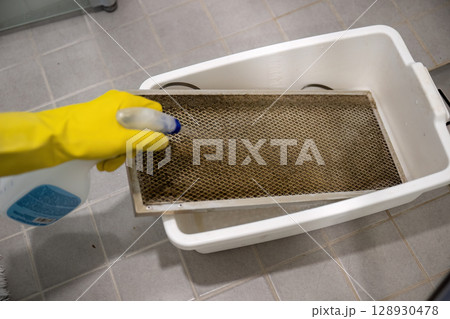 Cleaning dirty kitchen range hood grease filter with spray bottle and rubber gloves 128930478