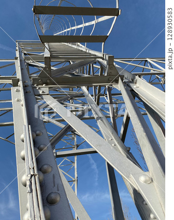 Looking up at metal transmission tower against blue sky with geometric patterns 128930583