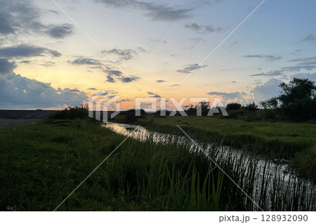 Beautiful river in meadow with colorful sky with sunset clouds Beautiful river in meadow with colorful sky with sunset clouds 128932090