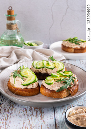 Appetizing sandwiches with cod liver pate, cucumber and arugula on a plate vertical view 128934960