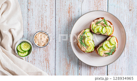 Homemade toasts with cod liver, cucumber and herbs on a plate on a table top view web banner 128934965