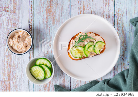 Cod liver, cucumber slices and arugula crostini on a plate on a table top view Cod liver, cucumber slices and arugula crostini on a plate on a table top view 128934969