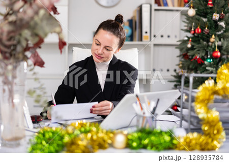 Portrait of successful business woman with New Years tinsel and Christmas tree in office 128935784