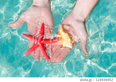 Hands starfish and seashell in tropical water 128936952