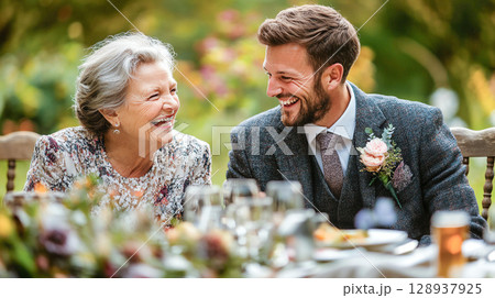 Mother and groom suit lunch dining table decorated by flowers at wedding ceremony celebration happiness smiling joyful event family together love bond cheerful emotional moment beautiful memories 128937925