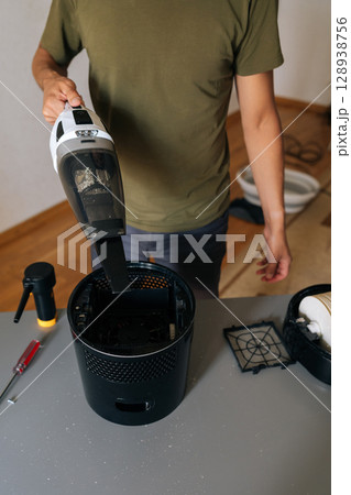 Vertical shot of cleaning company worker male cleaning air humidifier using handheld vacuum cleaner, performing thorough home device maintenance for optimal indoor air quality and cleanliness. Vertical shot of cleaning company worker male cleaning air humidifier using handheld vacuum cleaner, performing thorough home device maintenance for optimal indoor air quality and cleanliness. 128938756