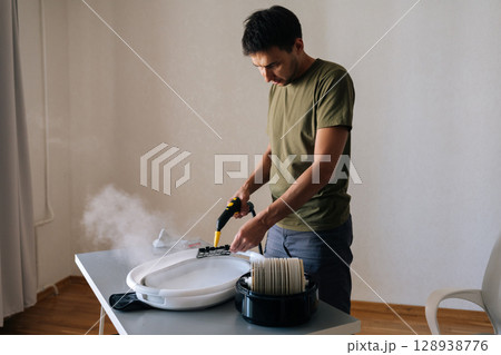 Portrait of focused professional cleaning air humidifier filter with steam cleaner, washing filter in basin for improved indoor air quality and device performance. Concept of cleaning and household. Portrait of focused professional cleaning air humidifier filter with steam cleaner, washing filter in basin for improved indoor air quality and device performance. Concept of cleaning and household. 128938776