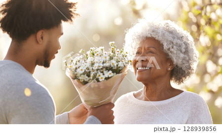 Mothers Day celebration with black woman receiving flower bouquet from her adult child 128939856