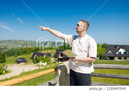 Smiling Man Pointing Ahead While Holding a Map in Mountain Village 128940340