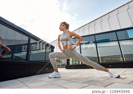 Young woman performing fitness stretching outdoors in a modern city setting Young woman performing fitness stretching outdoors in a modern city setting 128943048