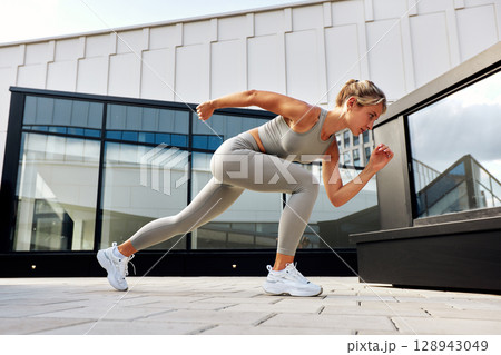 Young woman performing outdoor exercise wearing sporty attire on city rooftop terrace 128943049