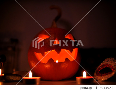 A carved Halloween pumpkin. Jack-o'-lantern glowing with a candle inside on a surface with lighting. Halloween festive spooky atmosphere concept 128943921