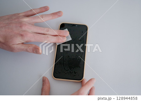 Man cleaning smartphone screen with dry wipe before applying screen protector Man cleaning smartphone screen with dry wipe before applying screen protector 128944858