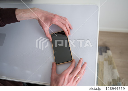 Man applying screen protector to smartphone on white desk Man applying screen protector to smartphone on white desk 128944859