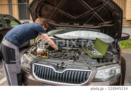 Man repairing car engine in residential outdoor parking area on a sunny summer day Man repairing car engine in residential outdoor parking area on a sunny summer day 128945214