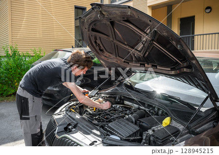 Man repairing car engine in residential outdoor parking area on a sunny summer day Man repairing car engine in residential outdoor parking area on a sunny summer day 128945215