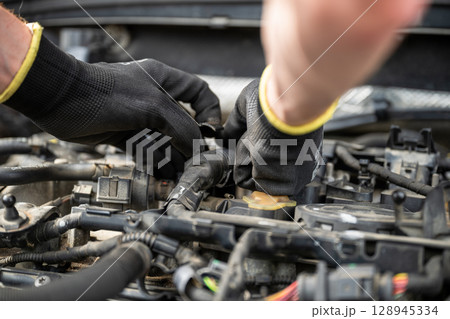 Mechanic wearing gloves fixing engine wiring inside car during repair Mechanic wearing gloves fixing engine wiring inside car during repair 128945334