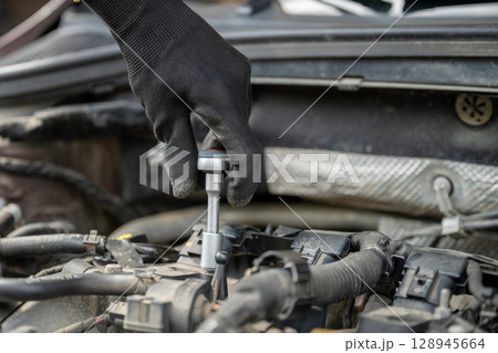 Mechanic hand in glove using socket wrench to repair car engine 128945664