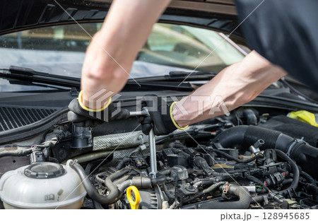 Man repairing car engine in residential outdoor parking area on a sunny summer day 128945685