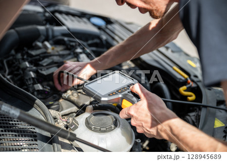 Mechanic using diagnostic tool to inspect car engine during vehicle maintenance 128945689