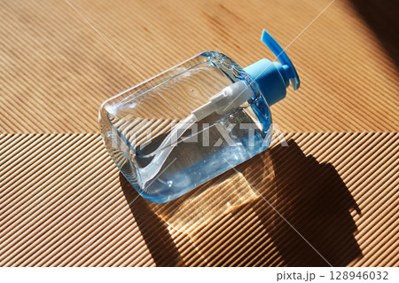 Hand washing gel in a blue bottle with a dispenser on a beige fluted background. 128946032