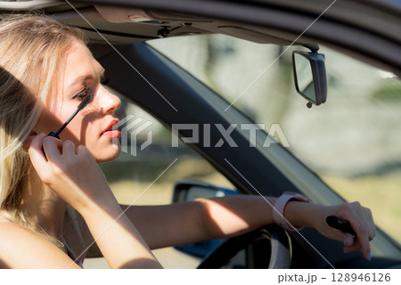 Woman applying mascara in car 128946126