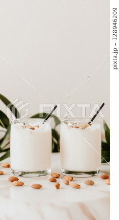 Almond milk drinks in glasses with straw on white surface, background Almond milk drinks in glasses with straw on white surface, background 128946209
