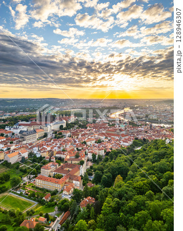 At sunrise, the stunning Prague Castle overlooks the city, with its impressive architecture illuminated by soft golden rays. The tranquil river and vibrant rooftops create a picturesque view. 128946307