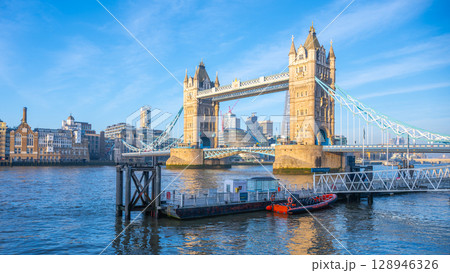 Morning at Tower Bridge reveals a stunning view with clear skies and soft light reflecting on the Thames River. The iconic structure stands majestically against the London skyline. 128946326