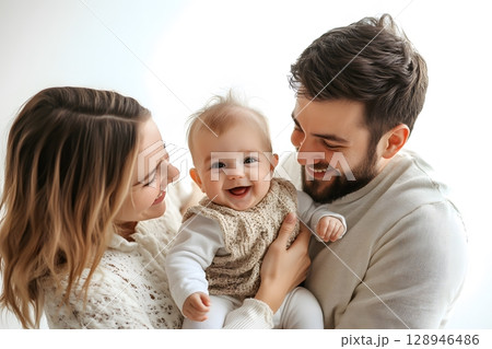 A mother and father lovingly hold their happy baby, all smiling brightly and enjoying a beautiful family moment together. 128946486