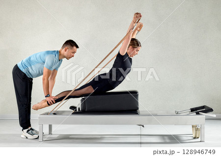 Woman practicing pilates with a trainer using a reformer in a studio 128946749