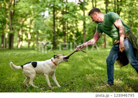 Playful interaction between a man and his dog in a forest 128946795