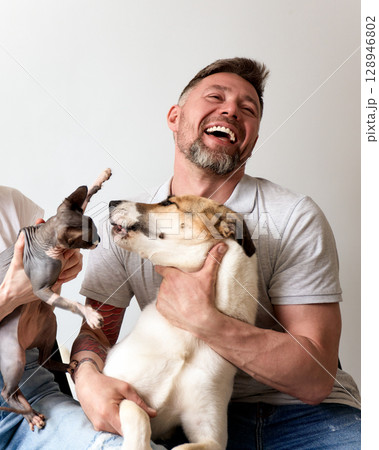 Man laughing while posing with a playful dog and a hairless cat Man laughing while posing with a playful dog and a hairless cat 128946802