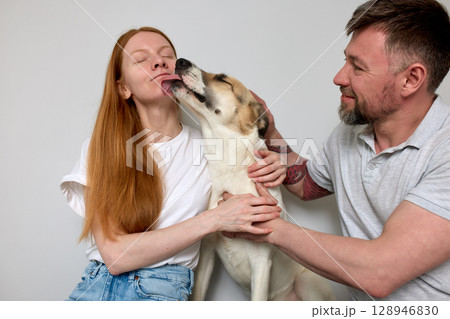 Young couple enjoying quality time with their affectionate pet dog indoors 128946830