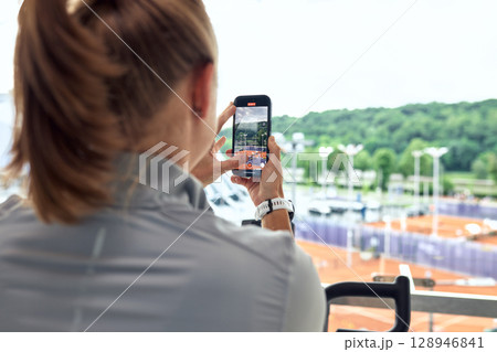 Woman capturing outdoor tennis courts with her smartphone from an elevated location 128946841