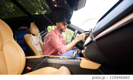 Stylish man driving a luxury car with beige interior on sunny day 128946860