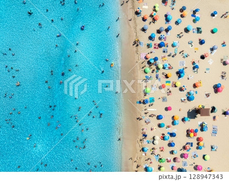 Aerial view of colorful umbrellas on sandy beach, swimming people Aerial view of colorful umbrellas on sandy beach, swimming people 128947343