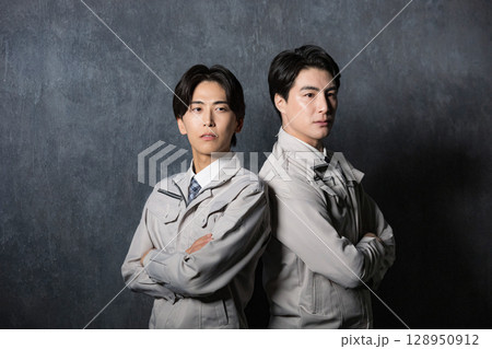 背中合わせで作業着で見上げる真剣な表情　グレーバックの男性2人 128950912